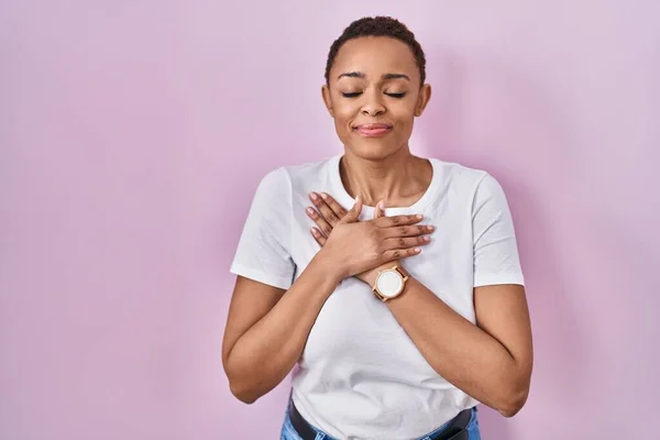 ピンクの背景の上に立つ美しいアフリカ系アメリカ人女性は 目を閉じて胸の上で手を笑顔で 顔に感謝のジェスチャー 健康の概念 — ストック写真