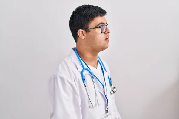 Young hispanic man with down syndrome wearing doctor uniform and stethoscope looking to side, relax profile pose with natural face with confident smile.