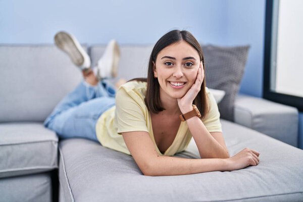 Молодая латиноамериканка, уверенно улыбающаяся, лежа дома на диване