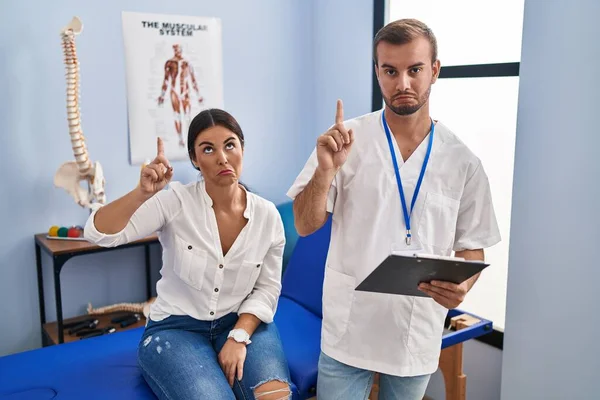 Young Hispanic Woman Physiotherapist Appointment Pointing Looking Sad Upset Indicating — Stockfoto