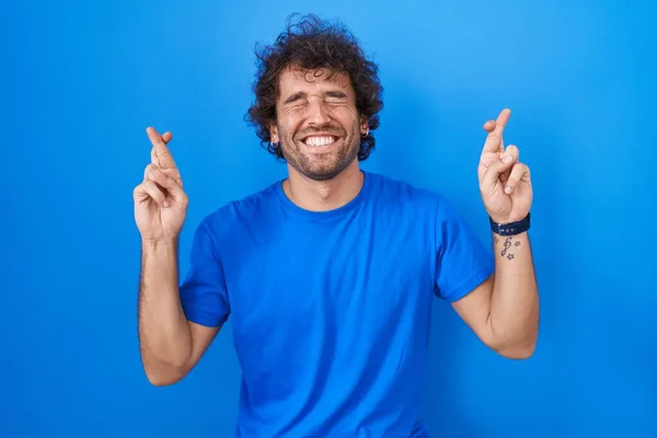 Hispanic Young Man Standing Blue Background Gesturing Finger Crossed Smiling — Stock Photo, Image