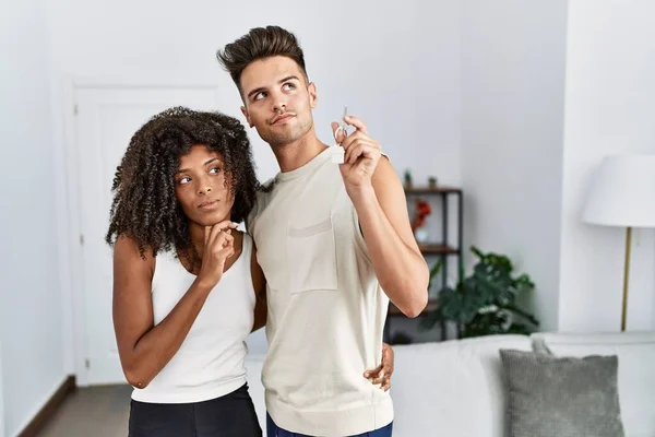 若い異人種間のカップル保持キーの新しい家深刻な顔の思考の質問について手で顎 思慮深い混乱のアイデア — ストック写真