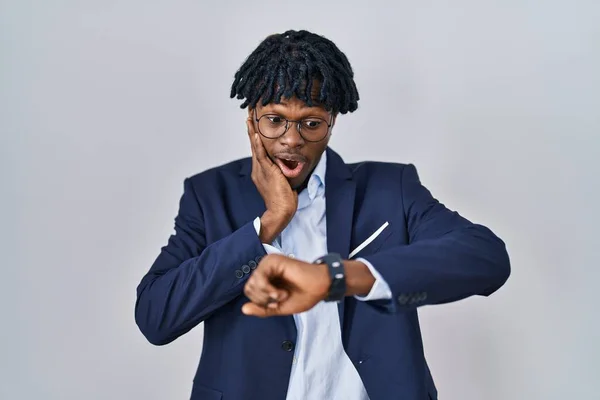 Young african man with dreadlocks wearing business jacket over white background looking at the watch time worried, afraid of getting late