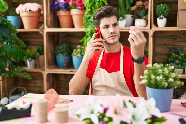 Young hispanic man florist talking on smartphone holding gift lace at flower shop