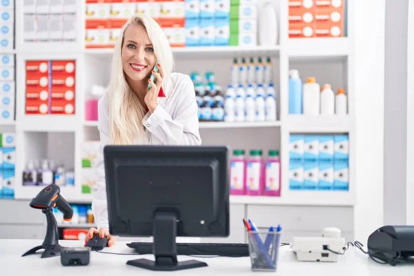 Joven Mujer Rubia Farmacéutica Hablando Teléfono Inteligente Utilizando Ordenador Farmacia — Foto de Stock