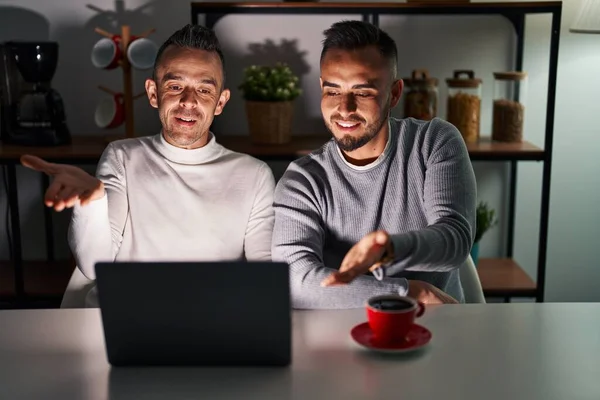 Homosexual couple using computer laptop smiling cheerful offering palm hand giving assistance and acceptance.