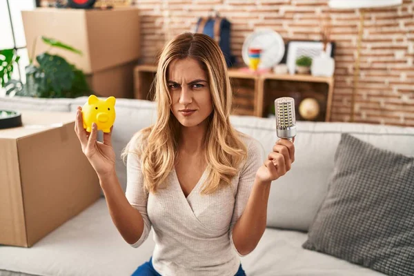 Young Blonde Woman Holding Led Bulb Piggy Bank Skeptic Nervous — Foto Stock