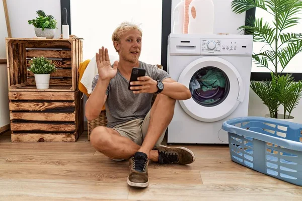 Genç Sarışın Adam Çamaşır Yıkıyor Akıllı Telefon Kullanıyor Merhaba Diyor — Stok fotoğraf