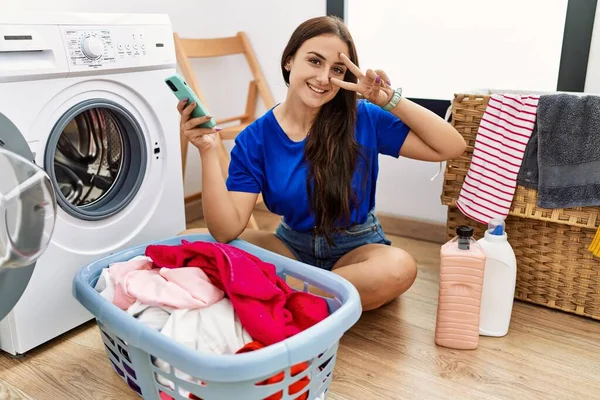 Ung Brunett Kvinna Gör Tvätt Med Smartphone Gör Fred Symbol — Stockfoto