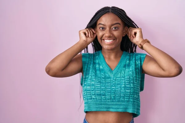 Young African American Braids Standing Pink Background Smiling Pulling Ears — Stockfoto