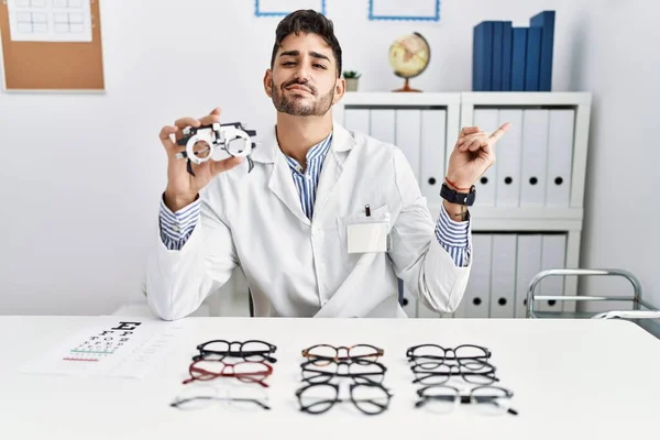 Young Optician Man Holding Optometry Glasses Pointing Hand Finger Side — Fotografia de Stock