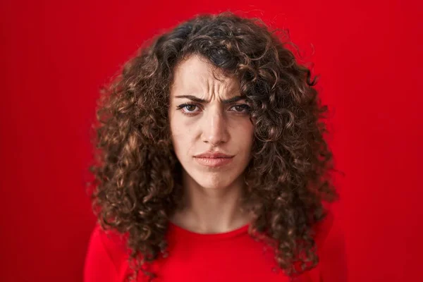 Kırmızı Arka Planda Duran Kıvırcık Saçlı Spanyol Kadın Şüpheci Gergin — Stok fotoğraf
