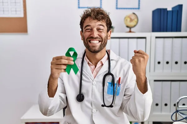 Young Hispanic Doctor Man Holding Support Green Ribbon Clinic Screaming — Stock Photo, Image