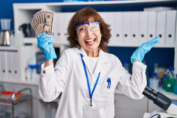 幸せな笑顔で勝利を祝うお金を保持している科学研究所で働く中年女性と手を上げと勝者の式 — ストック写真