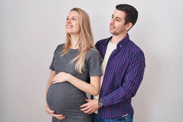 若いカップルの白い背景に離れて顔に笑顔で側に見て立って赤ちゃんを期待し 自然な表情 自信を持って — ストック写真