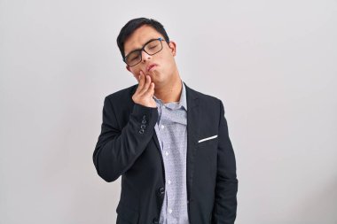 Down sendromlu genç İspanyol bir adam iş stili giyiniyor diş ağrısı ya da diş ağrısı yüzünden acı dolu bir ifadeyle ağıza dokunuyor. dişçi 