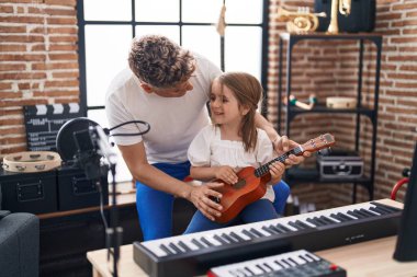 Baba ve kızı müzik stüdyosunda ukulele çalıyorlar.