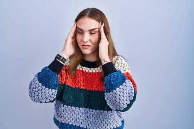 Young hispanic girl standing over blue background with hand on head, headache because stress. suffering migraine. 