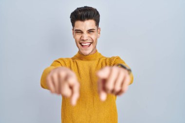Young hispanic man standing over blue background pointing to you and the camera with fingers, smiling positive and cheerful 
