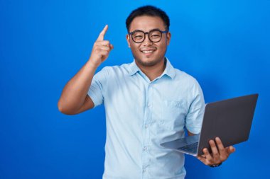 Chinese young man using computer laptop smiling amazed and surprised and pointing up with fingers and raised arms. 