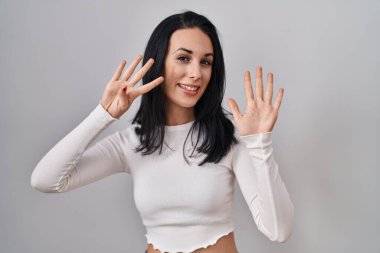 Hispanic woman standing over isolated background showing and pointing up with fingers number nine while smiling confident and happy. 