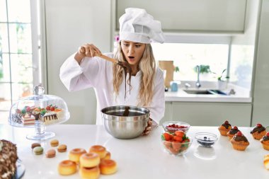 Young woman wearing cook uniform holding spoon with chocolate at kitchen