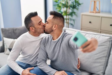 Two men couple make selfie by smartphone kissing at home