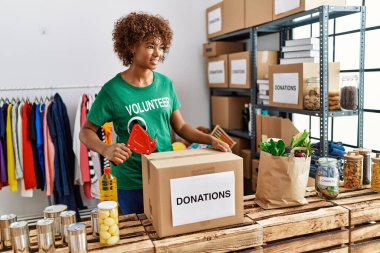 Gönüllü üniforma giyen genç Afrikalı Amerikalı kadın yardım merkezinde bağış kutusu paketliyor.