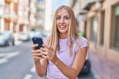 Sokakta akıllı telefon kullanan, kendine güvenen genç sarışın kadın.