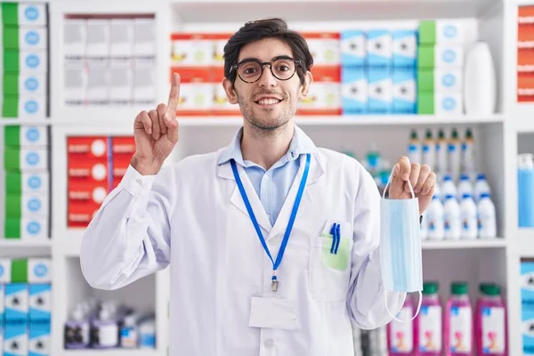 Young Hispanic Man Working Pharmacy Drugstore Holding Safety Mask Surprised — Foto de Stock