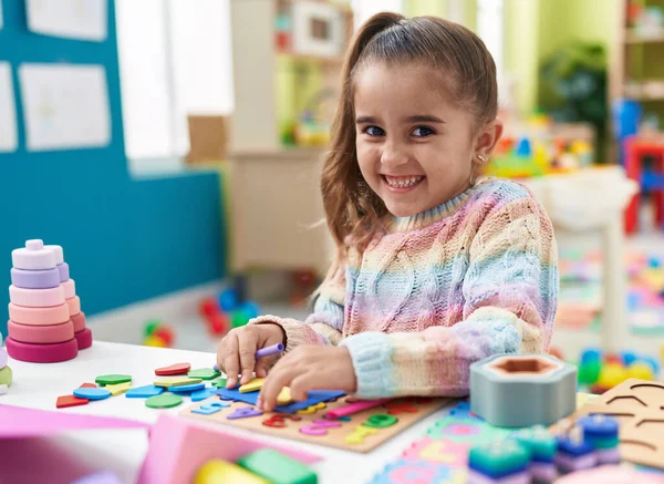 Adorable hispanic girl playing with maths puzzle game standing at kindergarten