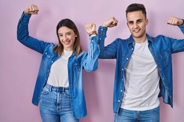Young Hispanic Couple Standing Pink Background Showing Arms Muscles Smiling — Stockfoto