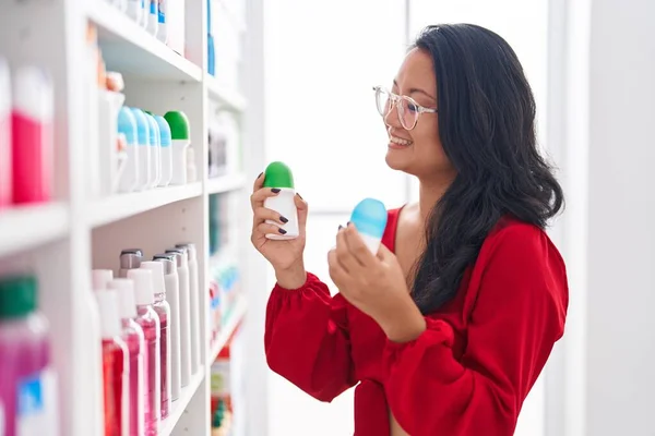 Young Chinese Woman Customer Smiling Confident Holding Deodorant Bottles Pharmacy — Stockfoto