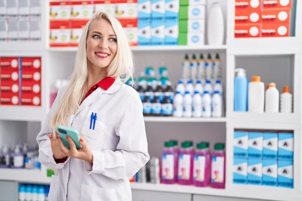 Young Blonde Woman Pharmacist Using Smartphone Working Pharmacy — Zdjęcie stockowe