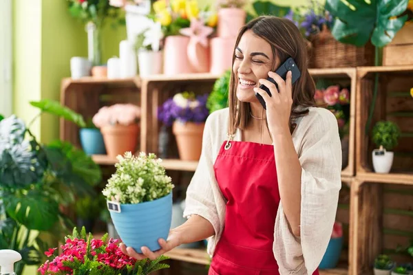 Young Beautiful Hispanic Woman Florist Talking Smartphone Holding Plant Flower — Stockfoto