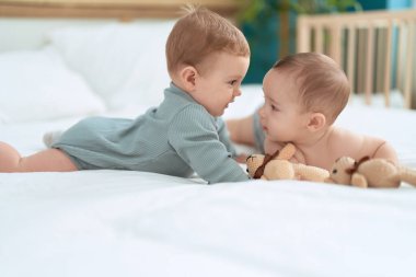 İki bebek yatak odasında oyuncak ayıyla oynuyorlar.