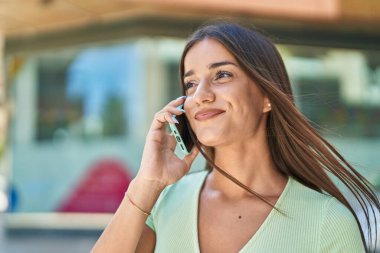 Genç, güzel, İspanyol bir kadın gülümsüyor ve caddede akıllı telefondan konuşuyor.