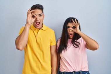 İzole edilmiş arka planda duran genç çift şaşırmış yüz ifadesiyle şaşırmış bir şekilde hareket ediyor ve parmaklarından bakıyor. İnançsız ifade. 