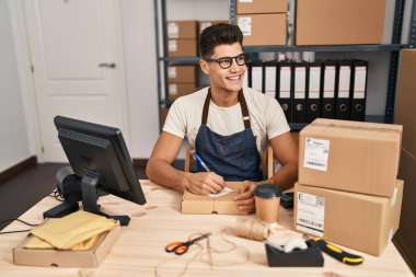 Latin kökenli genç bir iş adamı iş yerinde paket üzerine yazıyor.