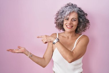 Pembe arka planda duran gri saçlı orta yaşlı kadın kameraya hayret ediyor ve gülümsüyor.. 