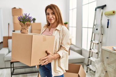 Karton kutu ve lavanta bitkisi taşıyan orta yaşlı beyaz bir kadın yeni evine taşınıyor..