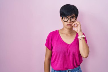Young asian woman with short hair standing over pink background mouth and lips shut as zip with fingers. secret and silent, taboo talking 