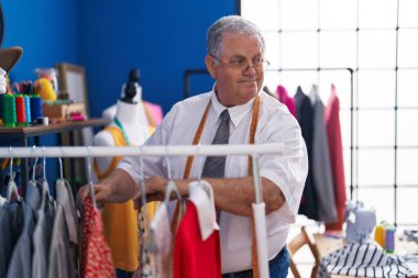 Orta yaşlı, gri saçlı, sırıtan, kendine güvenen, terzi dükkanında kendine güvenen bir adam.