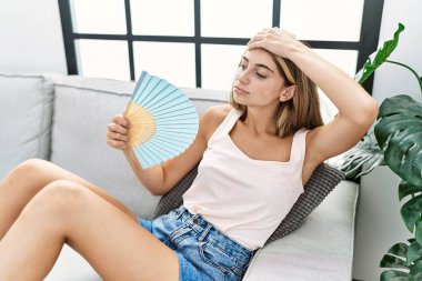 Beyaz bir kadın evde el fanı kullanıyor.