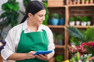 Young beautiful hispanic woman florist smiling confident using touchpad at flower shop