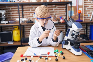 Sınıfta büyüteçle küçük sevimli bir öğrenci örneği arıyor.