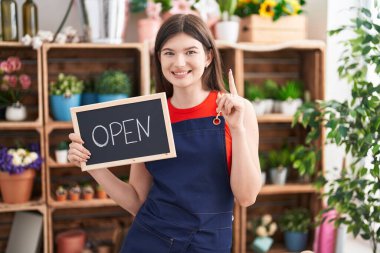 Young caucasian woman working at florist holding open sign surprised with an idea or question pointing finger with happy face, number one 