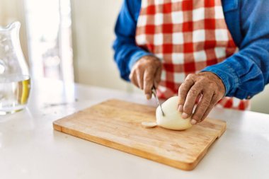 Kıdemli adam mutfakta soğan doğruyor.
