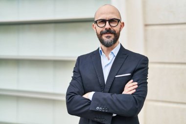 Kel genç bir iş adamı caddede kolları çapraz hareketlerle duruyor.