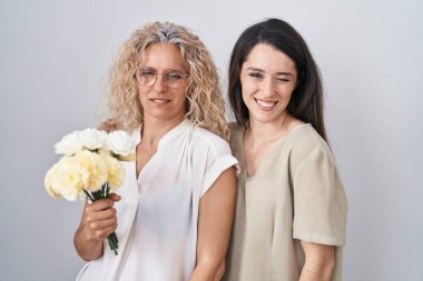 Bir buket beyaz çiçek tutan anne ve kız kameraya seksi bir ifadeyle bakıyor, neşeli ve mutlu bir yüzle.. 